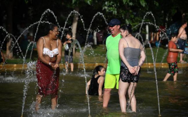 Un grupo de personas se refrescan en una fuente. Un grupo de personas se refrescan en una fuente.