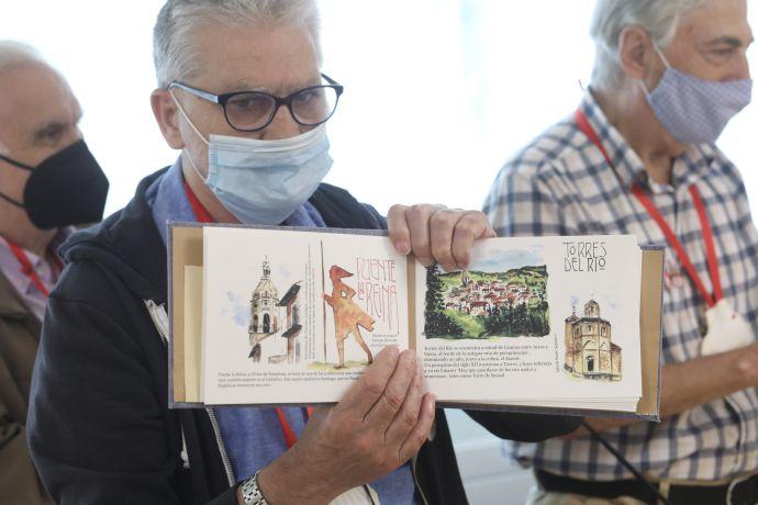 Uno de los residentes muestra el cuadernillo con ilustraciones al óleo de la llegada ficticia de los peregrinos a varios puntos del Camino de Santiago