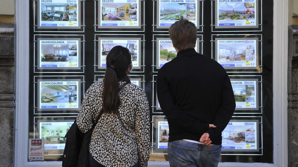 Dos jóvenes observan anuncios de venta de pisos en una inmobiliaria.
