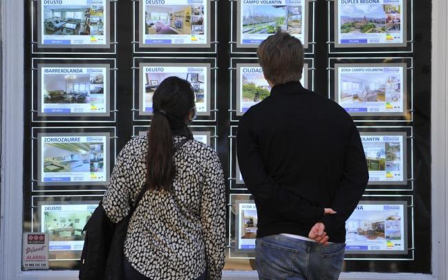 Dos jóvenes observan anuncios de venta de pisos en una inmobiliaria. Dos jóvenes observan anuncios de venta de pisos en una inmobiliaria.