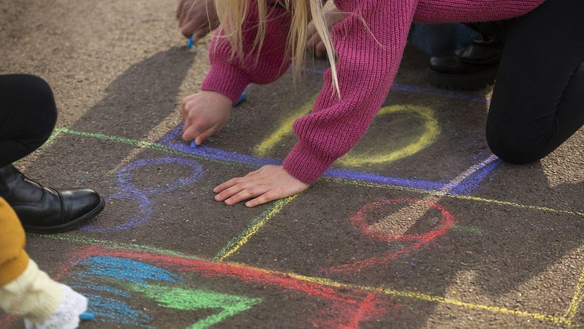 Una niña pinta en el suelo con tizas.