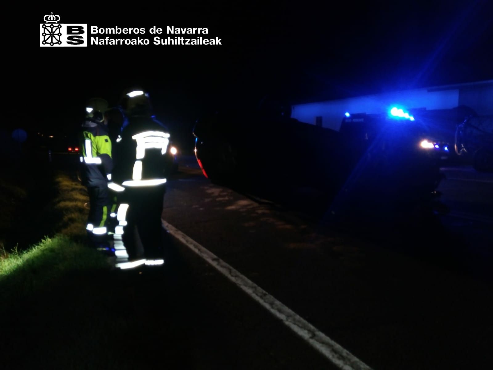 Imagen de dos de los bomberos junto al vehículo accidentado