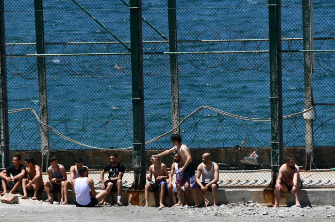Varios jóvenes migrantes marroquies esperan en las inmediaciones de la valla de la playa de Benzú, en Ceuta