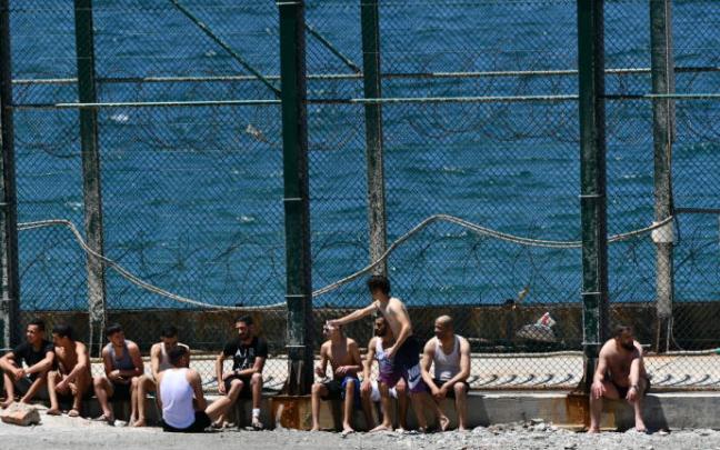 Varios jóvenes migrantes marroquies esperan en las inmediaciones de la valla de la playa de Benzú, en Ceuta