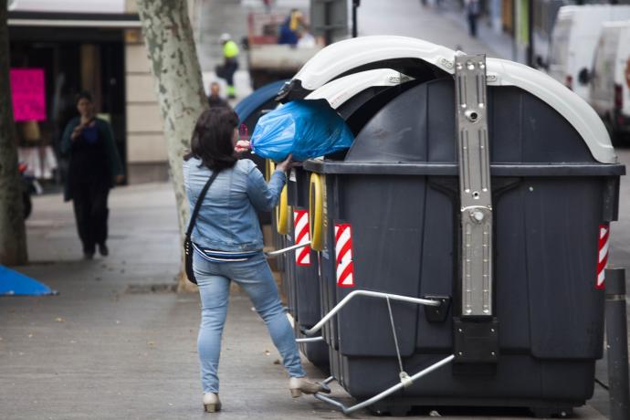 Una mujer -ajena a esta información- deposita una bolsa con residuos en un contenedor gris.