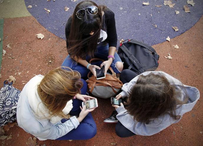 Varias menores se sientan juntas en un parque mientras utilizan sus móviles.