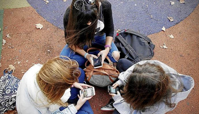 Varias menores se sientan juntas en un parque mientras utilizan sus móviles. Foto: Iban Aguinaga