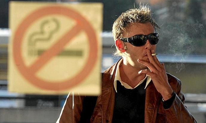 Un hombre fuma ante un cartel que prohíbe esa práctica. Foto: N.G.