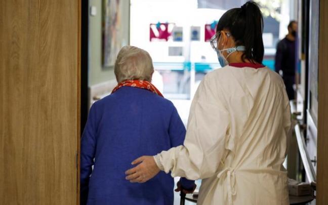 Una persona residente en un geriátrico es acompañada por su cuidadora.