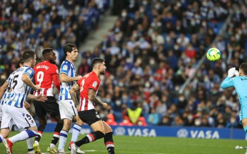 Álex Remiro intenta despejar, sin éxito, el lanzamiento de falta de Muniain.