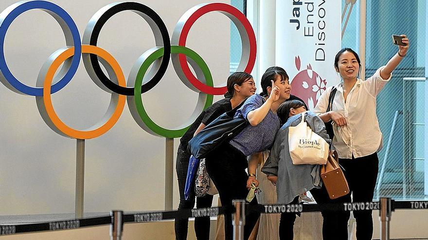 Visitantes se toman un selfie con el monumento de los Anillos Olímpicos en el aeropuerto internacional de Tokio, en Haneda, de fondo.