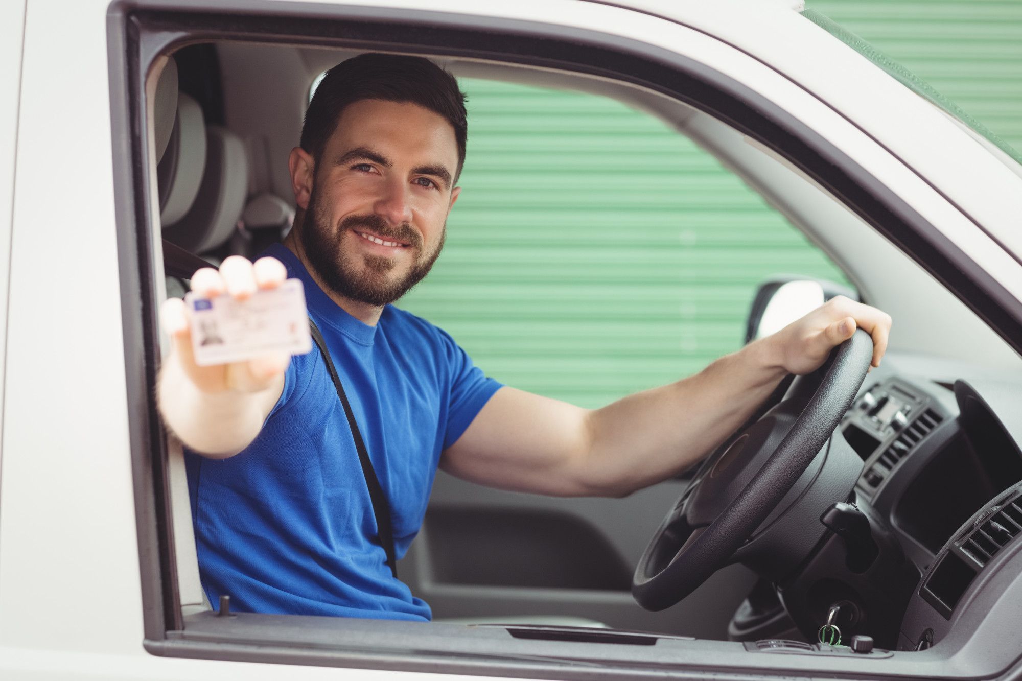 Un hombre al volante de su coche muestra su carné.