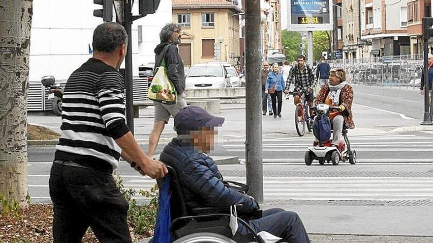 Una persona mayor en silla de ruedas con su cuidador.