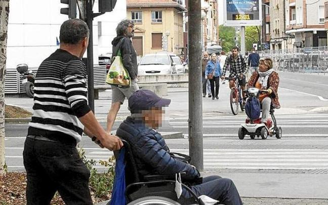 Una persona mayor en silla de ruedas con su cuidador.