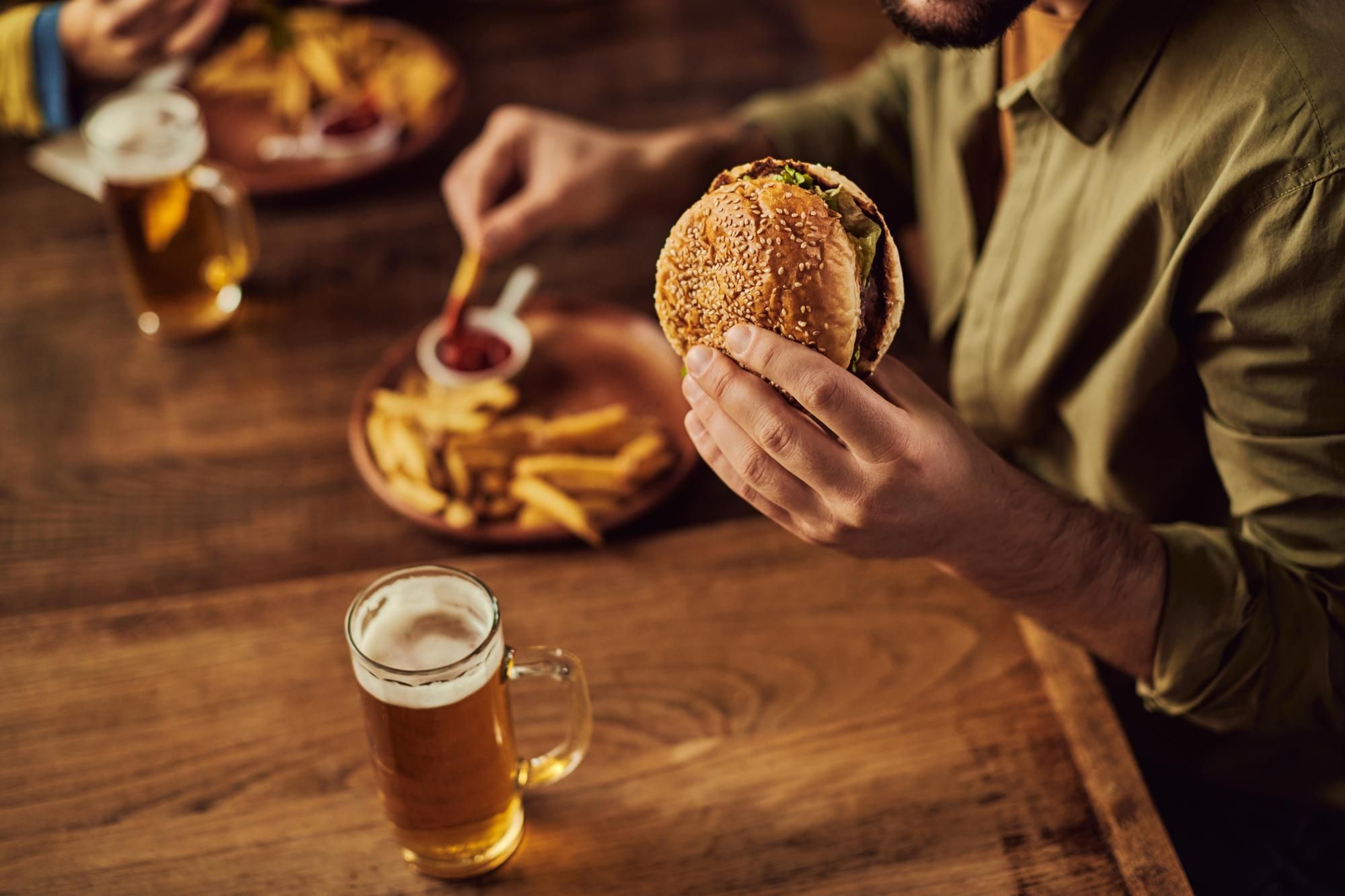 Un hombre toma una hamburguesa con patatas, acompañada de una cerveza.