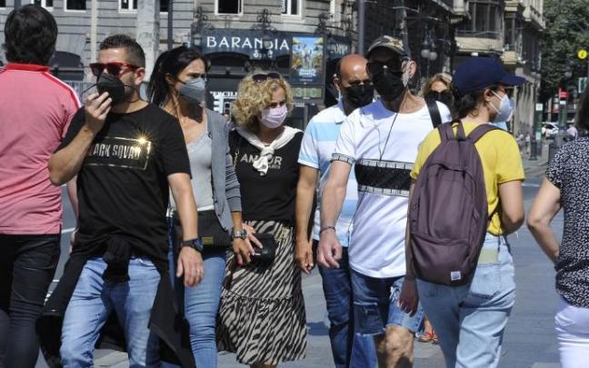 Varias personas paseando por la calle con mascarilla.