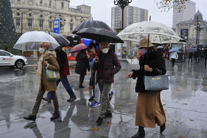 Varias personas caminan bajo la lluvia con paraguas.