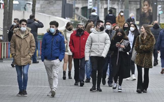 Varias personas pasean por la calle con mascarilla.