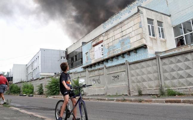 Un ni&ntilde;o mira una columna de humo que se eleva sobre un almac&eacute;n comercial e industrial en Odesa.