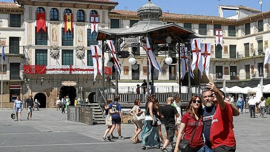 Tres amigos se hacen una fotografía, con el kiosco y la Casa del Reloj decorados, de fondo, donde hoy comenzarán las fiestas de Tudela.