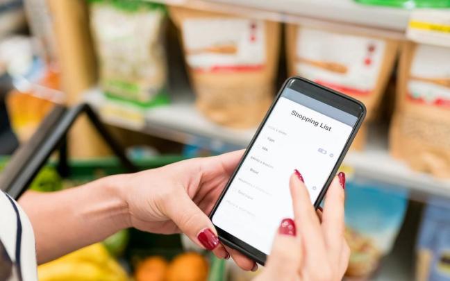 Una mujer utiliza una lista de compra digital en un supermercado. Una mujer utiliza una lista de compra digital en un supermercado.