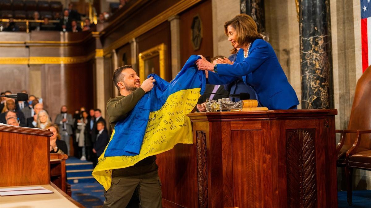 El presidente de Ucrania, Volodimir Zelenski, entrega a la presidenta de la Cámara de Representantes de Estados Unidos, Nancy Pelosi, una bandera de Ucrania.