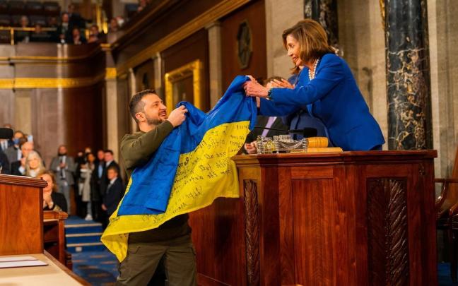 El presidente de Ucrania, Volodimir Zelenski, entrega a la presidenta de la C&aacute;mara de Representantes de Estados Unidos, Nancy Pelosi, una bandera de Ucrania.