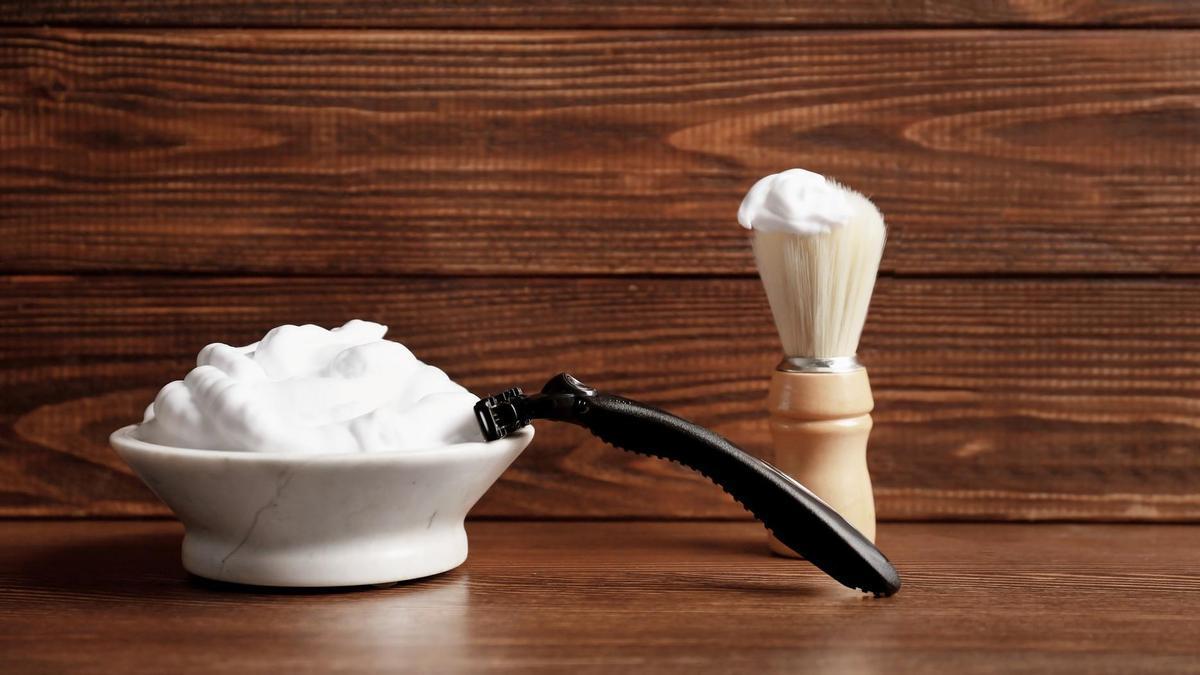 Un bol con espuma de afeitar junto a una brocha y una cuchilla.