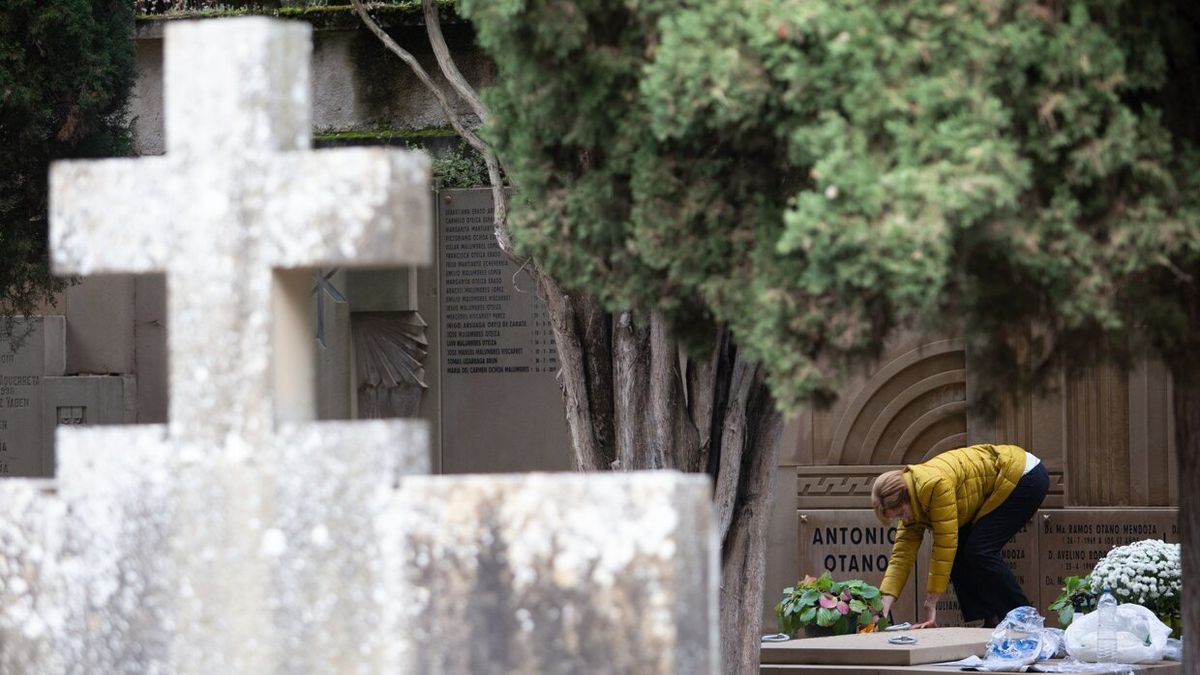 Una mujer deja flores en una tumba en el cementerio de Pamplona.