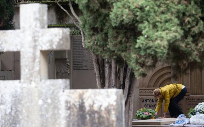 Una mujer deja flores en una tumba en el cementerio de Pamplona.