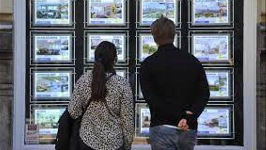 Dos personas observan anuncios de venta de pisos en una inmobiliaria