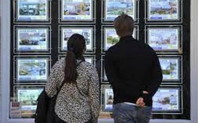 Dos personas observan anuncios de venta de pisos en una inmobiliaria Dos personas observan anuncios de venta de pisos en una inmobiliaria