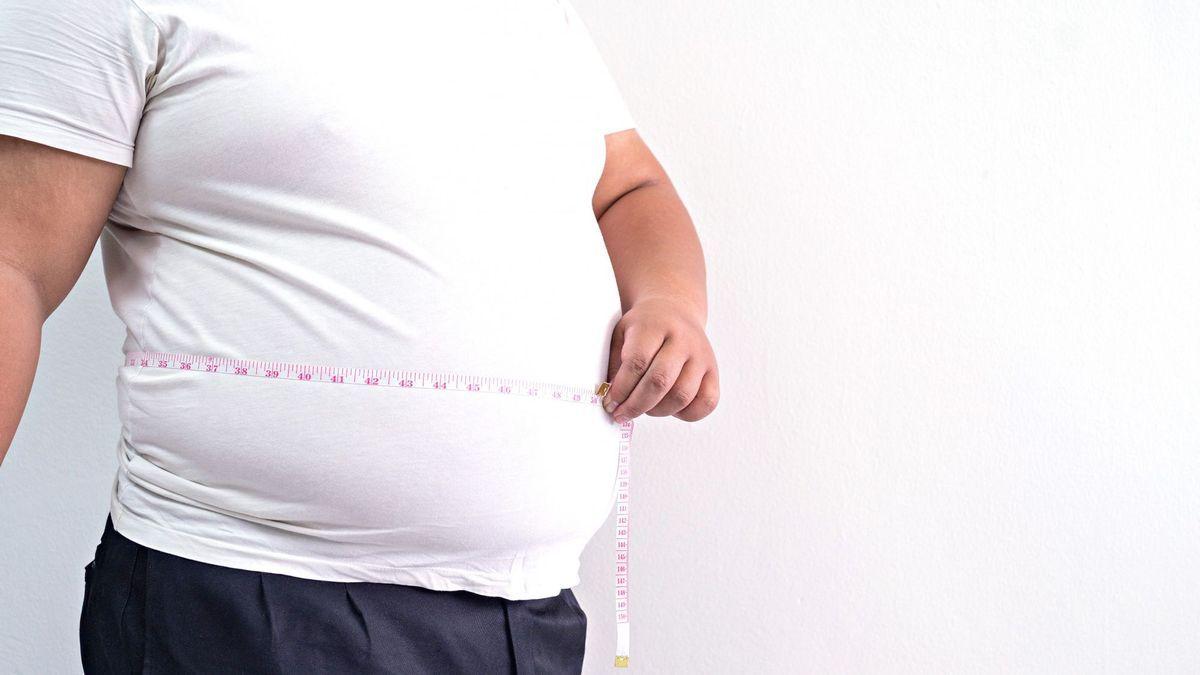 Un hombre obeso mide su cintura con una cinta métrica.