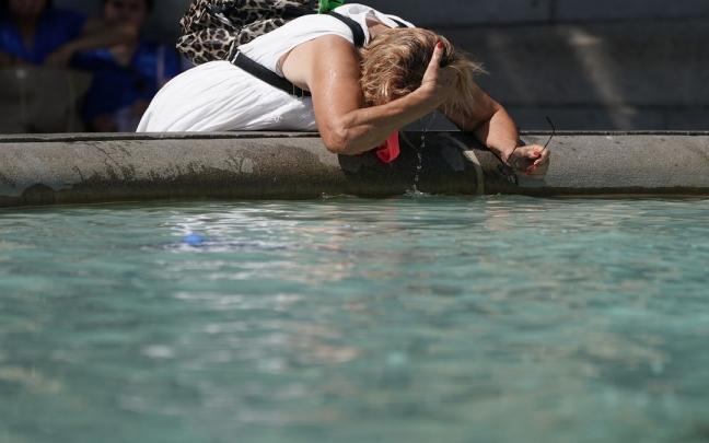 Una mujer se refresca en una fuente para combatir el calor Una mujer se refresca en una fuente para combatir el calor