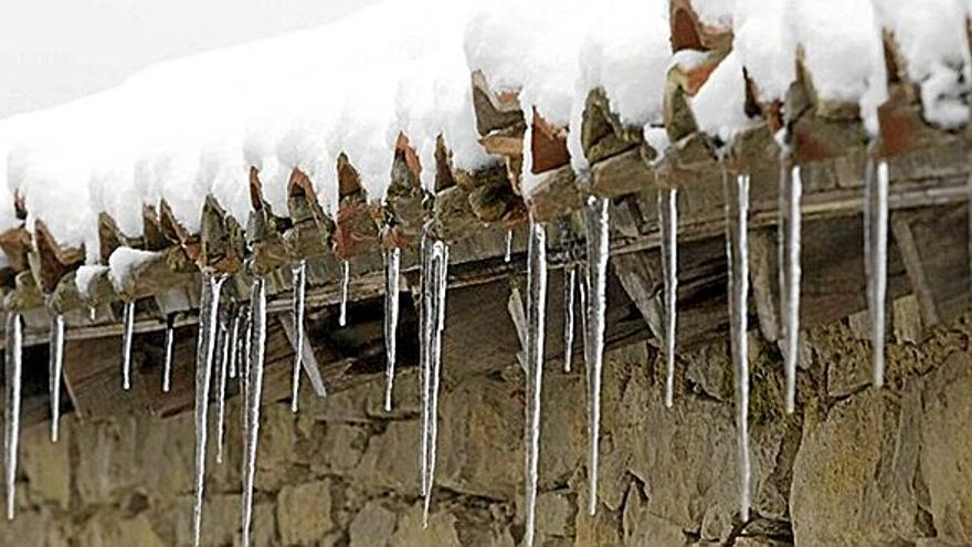 Carámbanos de hielo cuelgan del alero de una casa con un tejado cargado de nieve como consecuencia de un temporal pasado que azotó al territorio.