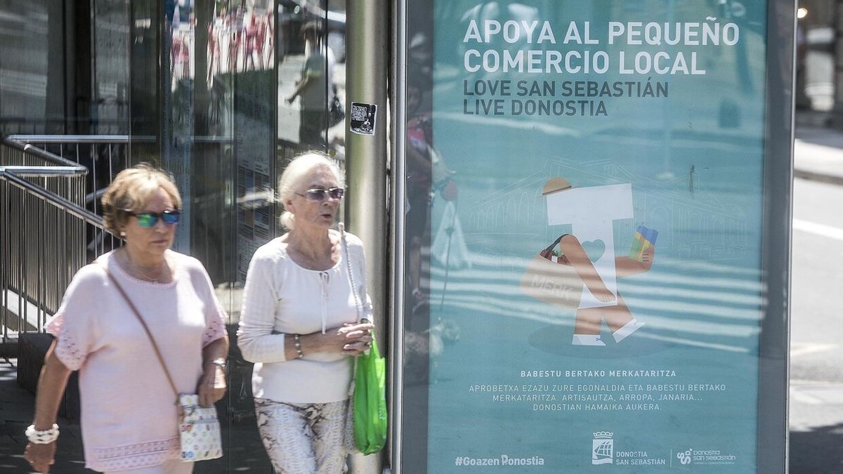 Dos mujeres pasan junto a un anuncio del comercio local.