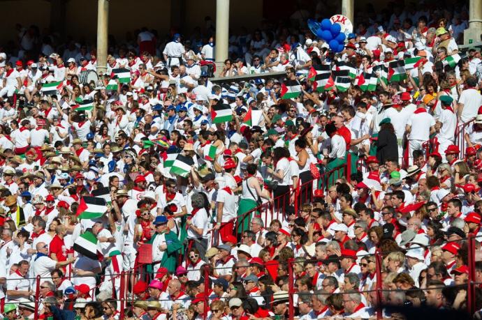 Ambiente en el tendido de sol durante la corrida del día 9 con toros de la ganadería de José Escolar: varios mozos levantan banderas de Palestina en la zona de la peña Alegría de Iruña.