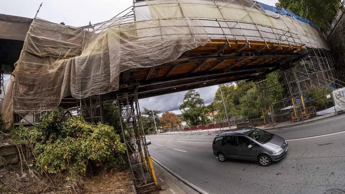 Un vehículo pasa por debajo de la pasarela, tapada por una lona.