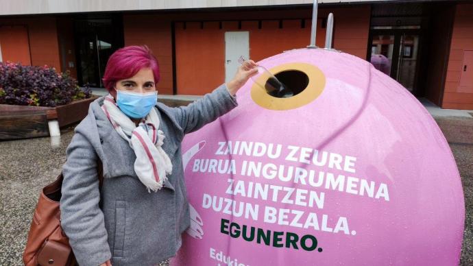 Una mujer tirando una botella en un contenedor de vidrio de color rosa, como iniciativa de la lucha contra el cáncer de mama.