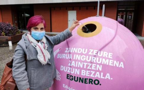 Una mujer tirando una botella en un contenedor de vidrio de color rosa, como iniciativa de la lucha contra el cáncer de mama.