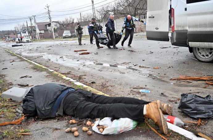 Varios ucranianos portan una bolsa para trasladar cadáveres mientras hay otro cuerpo tendido en el suelo, Bucha.