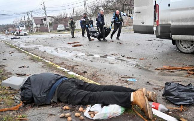 Varios ucranianos portan una bolsa para trasladar cadáveres mientras hay otro cuerpo tendido en el suelo, Bucha.