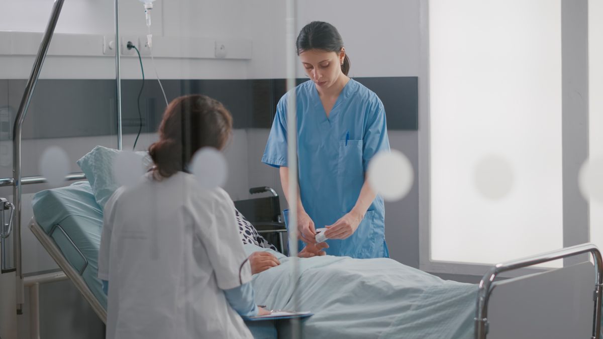 Dos sanitarias atienden a una paciente en la cama de un hospital.