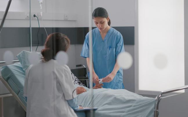 Dos sanitarias atienden a una paciente en la cama de un hospital.