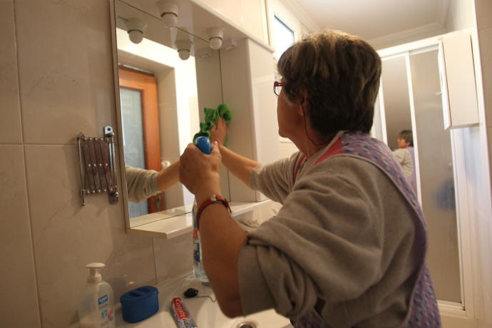 Una mujer limpiando el espejo de un baño.