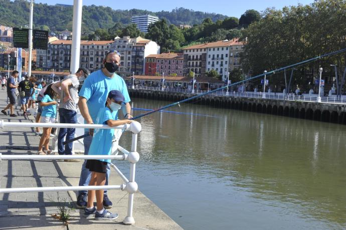 Un padre acompaña a su hijo que participa en la Escuela de Pesca Gran Ría de Bilbao en el muelle de Ripa.