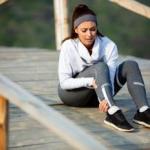 Una mujer vestida con ropa de deporte se duele del tobillo.