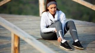 Una mujer vestida con ropa de deporte se duele del tobillo.