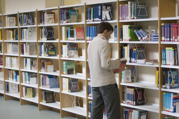 Un estudiante universitario ojeando unos libros en el interior de la biblioteca de la UPV