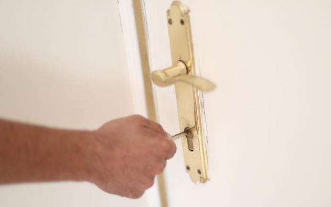 Un hombre introduce una llave en la cerradura de la puerta de una vivienda.